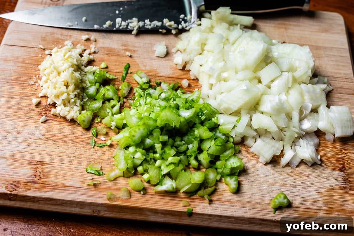 Grandma Georgia's Homestyle Chicken and Rice Bake 13 Finely chopped onion, celery, and minced garlic neatly arranged on a wooden cutting board, with a chef's knife in the background, signaling preparation for the casserole's aromatic base.