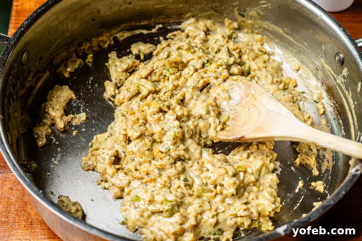 Grandma Georgia's Homestyle Chicken and Rice Bake 16 A wooden spoon stirs the mixture of flour, Zoup! bone broth base, and vegetables in a metal pan, combining the rich flavors into a developing sauce for the chicken and rice casserole.