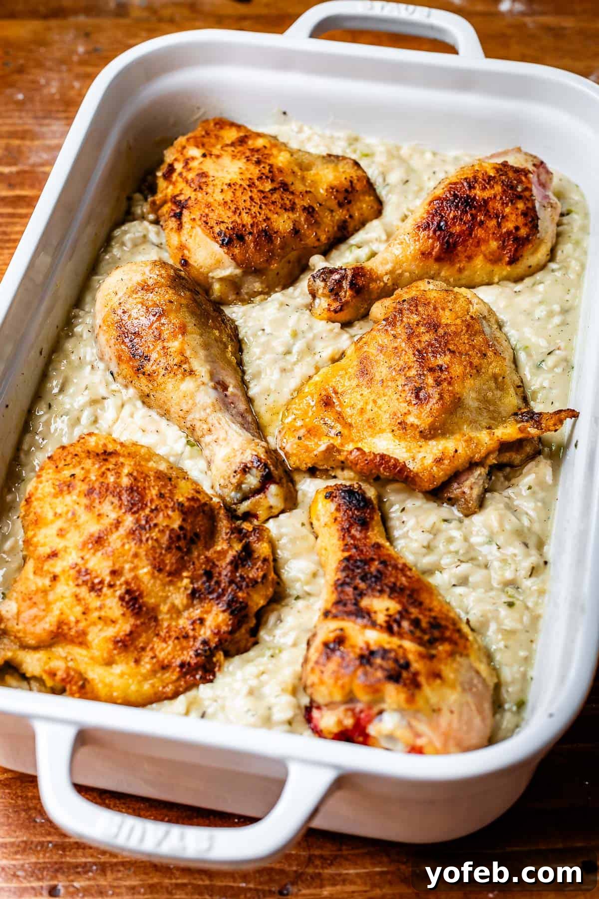 Grandma Georgia's Homestyle Chicken and Rice Bake 17 Seared chicken pieces are carefully arranged, nestled into a creamy mixture of uncooked rice and homemade white sauce within a casserole dish, ready for baking.