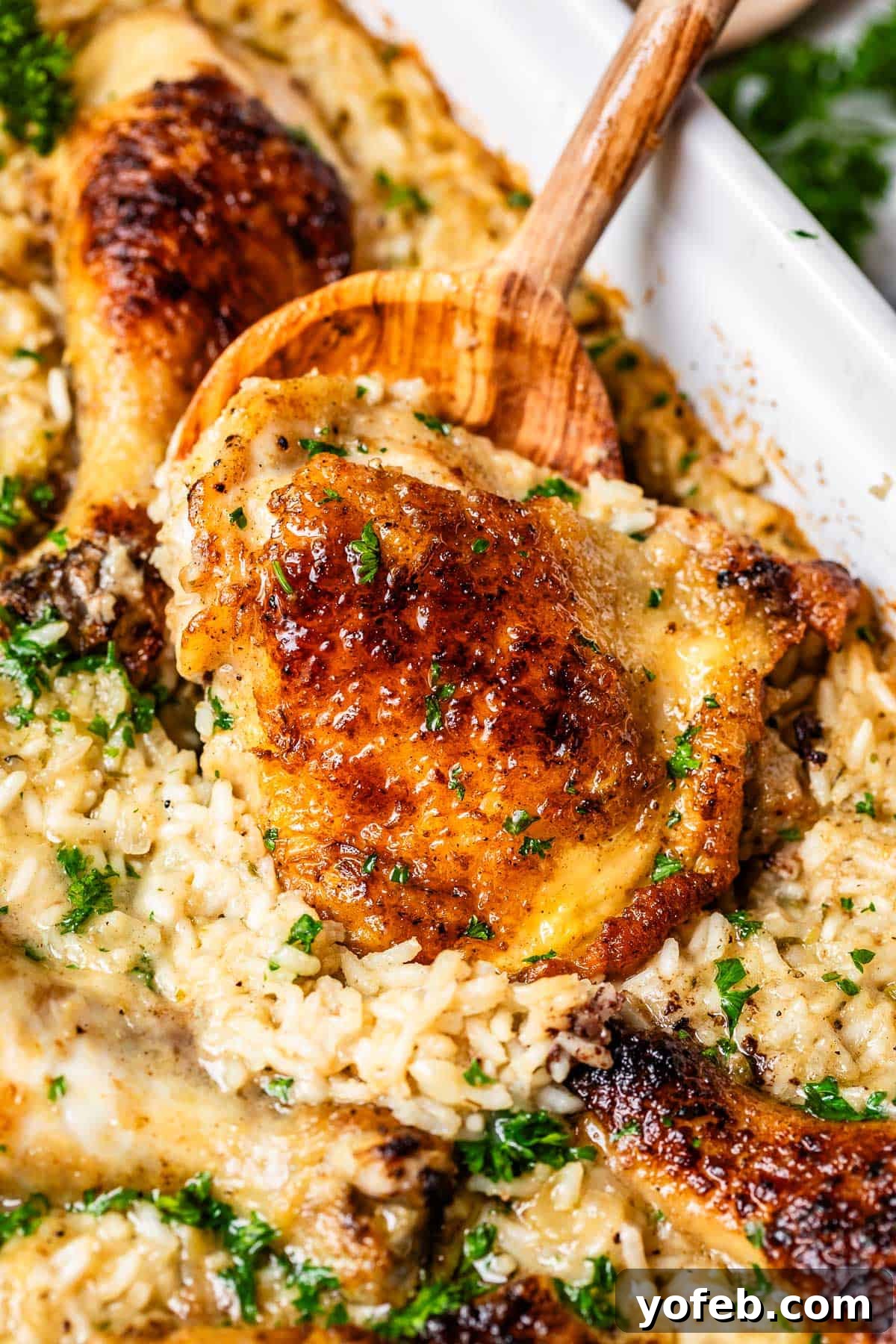Grandma Georgia's Homestyle Chicken and Rice Bake 3 A wooden spoon carefully scoops a tender, cooked chicken thigh from a bed of perfectly creamy rice within a warm casserole dish. This image captures the essence of a comforting, old-fashioned chicken and rice casserole, updated for the modern kitchen but retaining all its nostalgic charm.