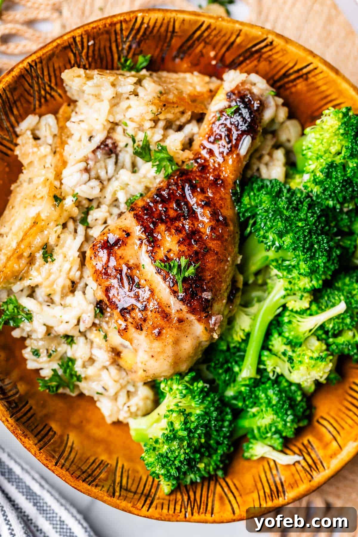 Grandma Georgia's Homestyle Chicken and Rice Bake 7 A close-up shot of a ceramic bowl filled with creamy rice, a cooked chicken drumstick, and fresh broccoli. The golden, crispy rice bits around the edges are visible, showcasing the delicious texture achieved in this homemade casserole.