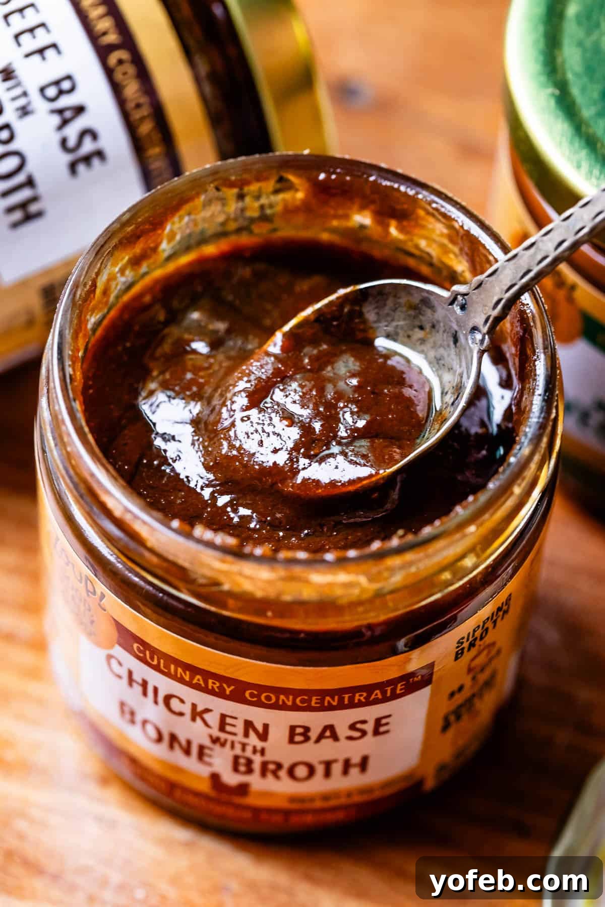 Grandma Georgia's Homestyle Chicken and Rice Bake 8 A spoon dips into a jar of rich, golden chicken broth base concentrate, artfully placed on a wooden table, highlighting the product's quality and texture.