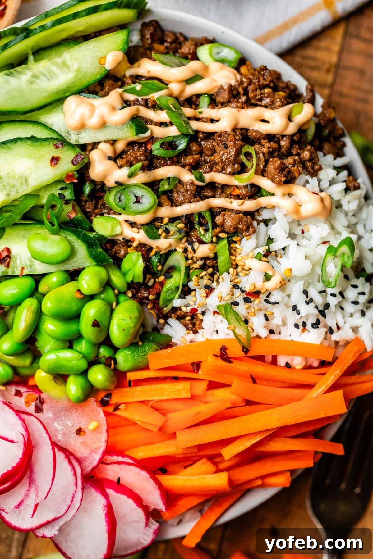 Easy 30-Minute Korean Beef 2 A vibrant Korean beef bowl overflowing with fluffy white rice, savory ground beef, colorful fresh vegetables, and a generous drizzle of creamy Sriracha mayo, topped with toasted sesame seeds.