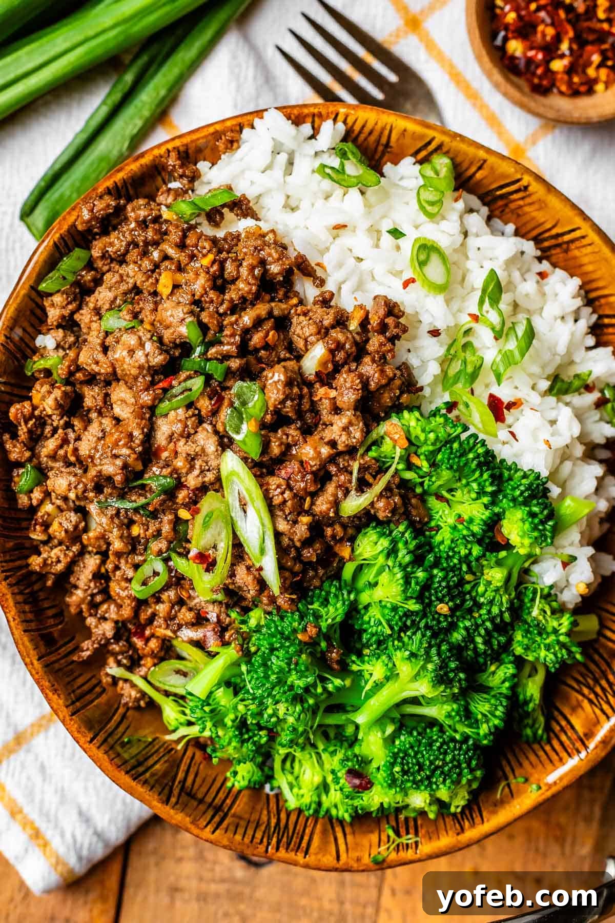 Easy 30-Minute Korean Beef 4 A rustic brown ceramic bowl filled with perfectly steamed rice, tender florets of broccoli, and a generous portion of savory Korean beef, all garnished with fresh green onions.