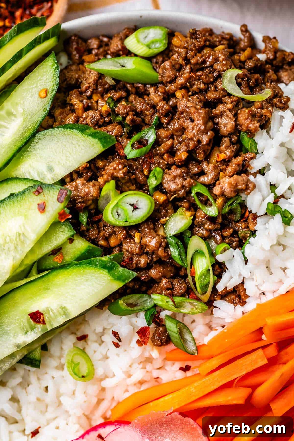 Easy 30-Minute Korean Beef 5 A close-up view of a Korean beef bowl featuring perfectly seasoned ground beef, fluffy rice, crisp cucumber slices, and vibrant matchstick carrots, ready to be enjoyed.