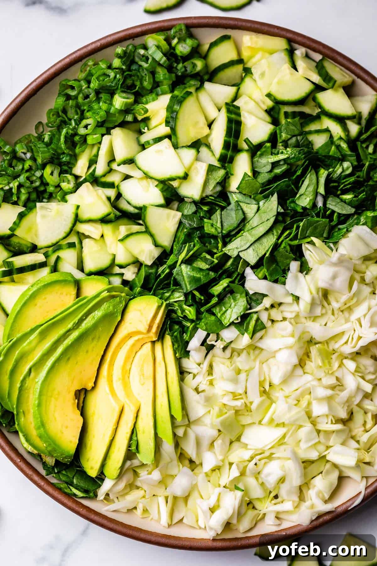 The Ultimate Green Goddess Salad 14 chopped green onion, cucumber, spinach, cabbage, and avocado lined up on a plate.