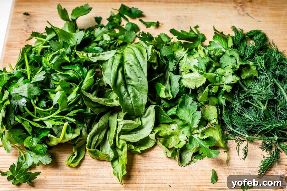 The Ultimate Green Goddess Salad 7 parsley, basil, cilantro, and dill lined up on a wooden cutting board to be chopped.