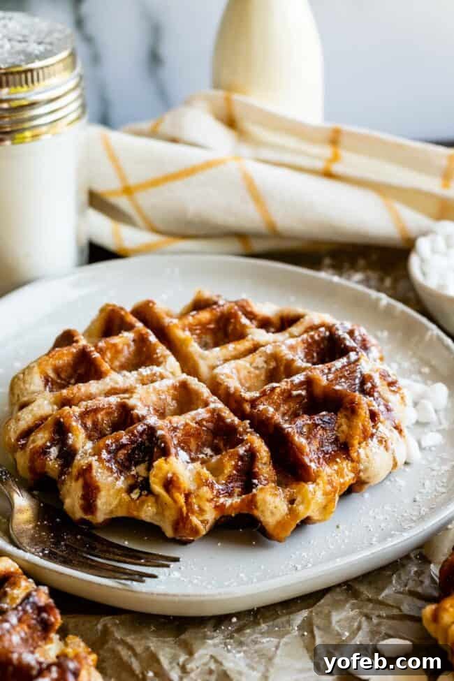 Pearl Sugar Liege Waffles A fluffy Liege waffle dusted with powdered sugar and sprinkled with extra pearl sugar on a white plate, ready to be enjoyed.