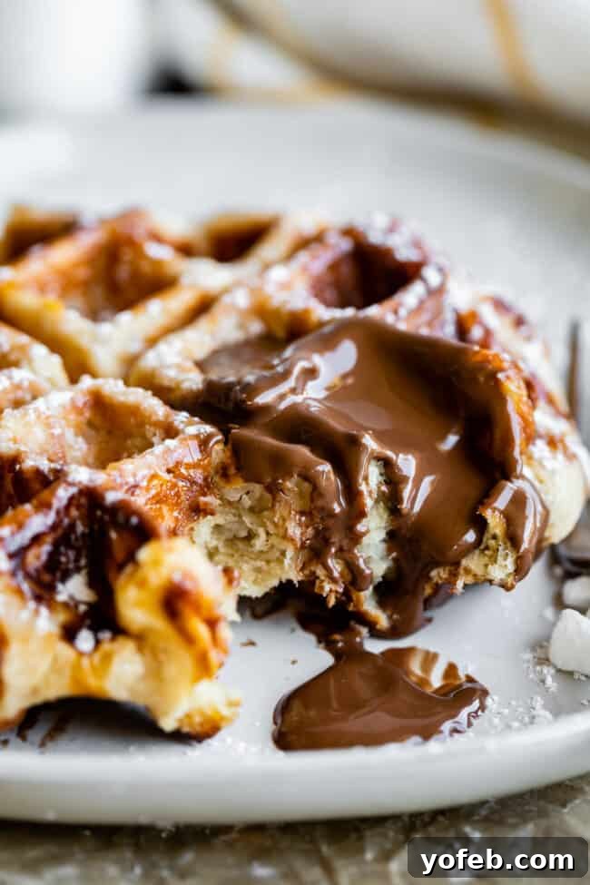 Liege Waffle with Nutella and Pearl Sugar A freshly made Liege waffle on a plate, adorned with a luscious drizzle of melted Nutella, and a scattering of pearl sugar nearby.