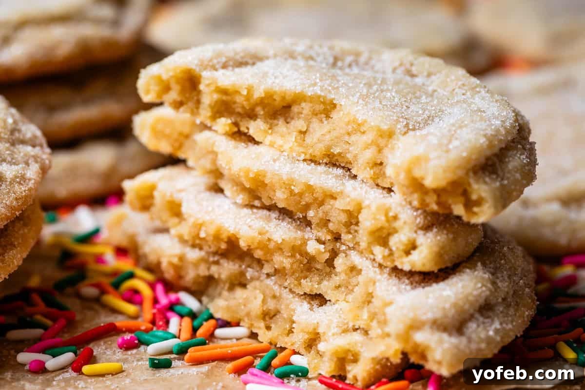 No Roll Chewy Sugar Cookies 30 Minute Recipe 21 Four stacked halves of drop sugar cookies, resting on a bed of colorful sprinkles on parchment paper.