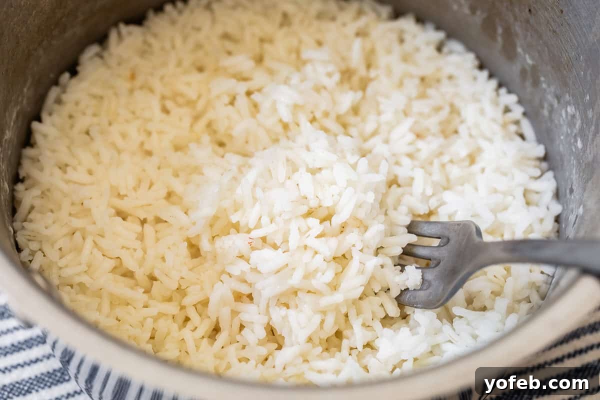 Perfect Stovetop Rice Every Time 12 Fluffing freshly cooked rice in a pot with a fork, creating a light and airy texture.