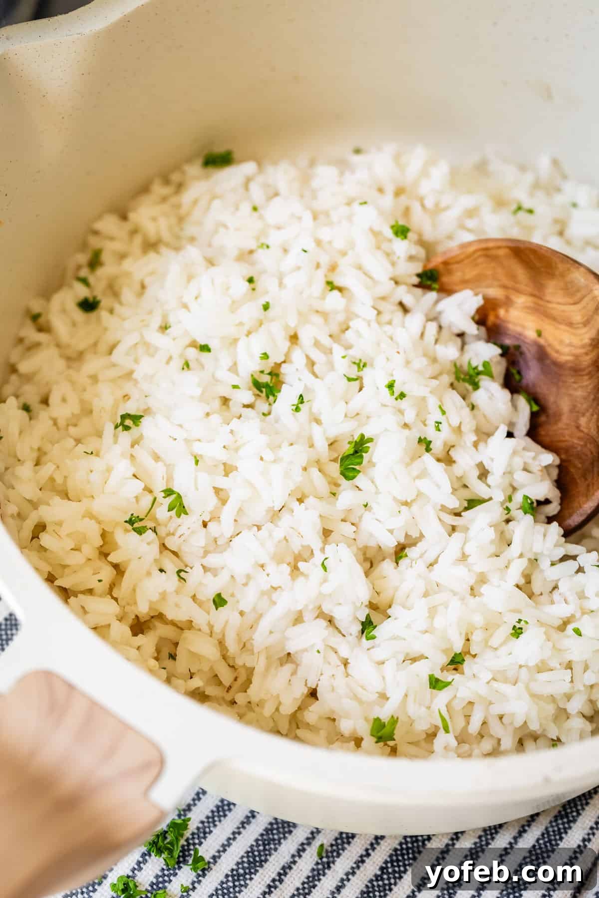 Perfect Stovetop Rice Every Time 4 Close up of perfectly cooked white rice in a white pot with a wooden spoon and fresh parsley garnish.