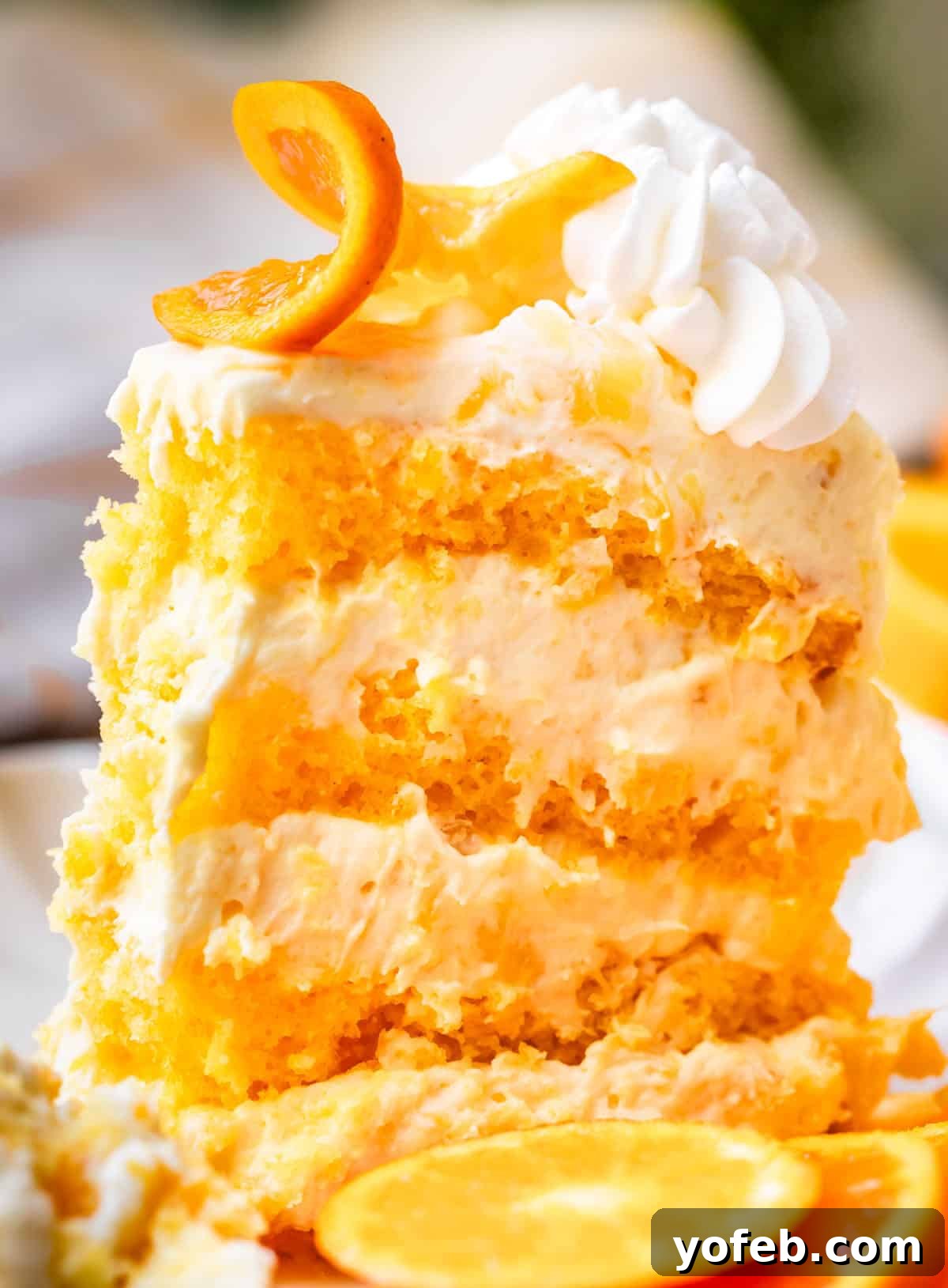 Golden Pineapple Mandarin Cake 21 side view of a tall piece of sunshine cake with 8 layers, garnished with an orange slice.