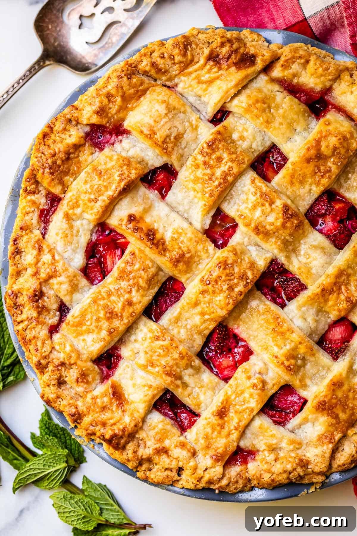 Summer's Sweet & Tart Strawberry Rhubarb Pie 3 vertical shot of a whole, baked, lattice crust strawberry rhubarb pie with a serving pie serving spoon.