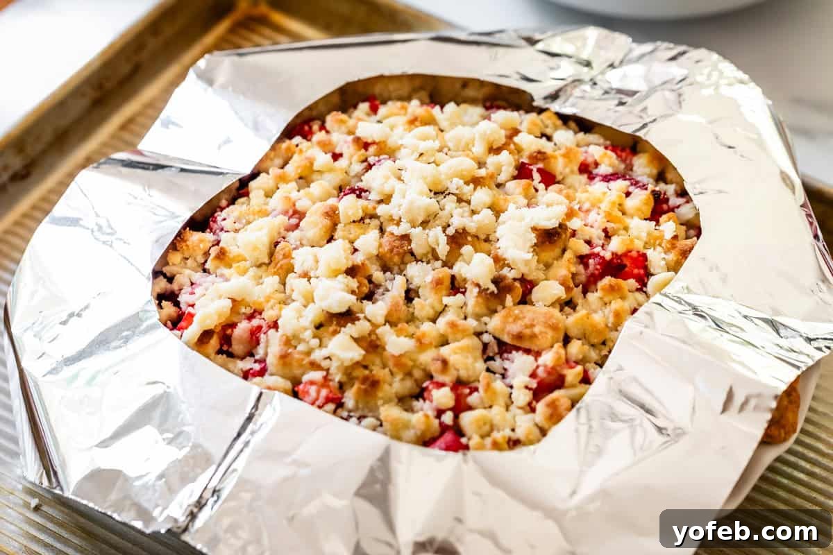 Summer's Sweet & Tart Strawberry Rhubarb Pie 24 strawberry rhubarb pie with crumble topping with crust protected by a foil shield.