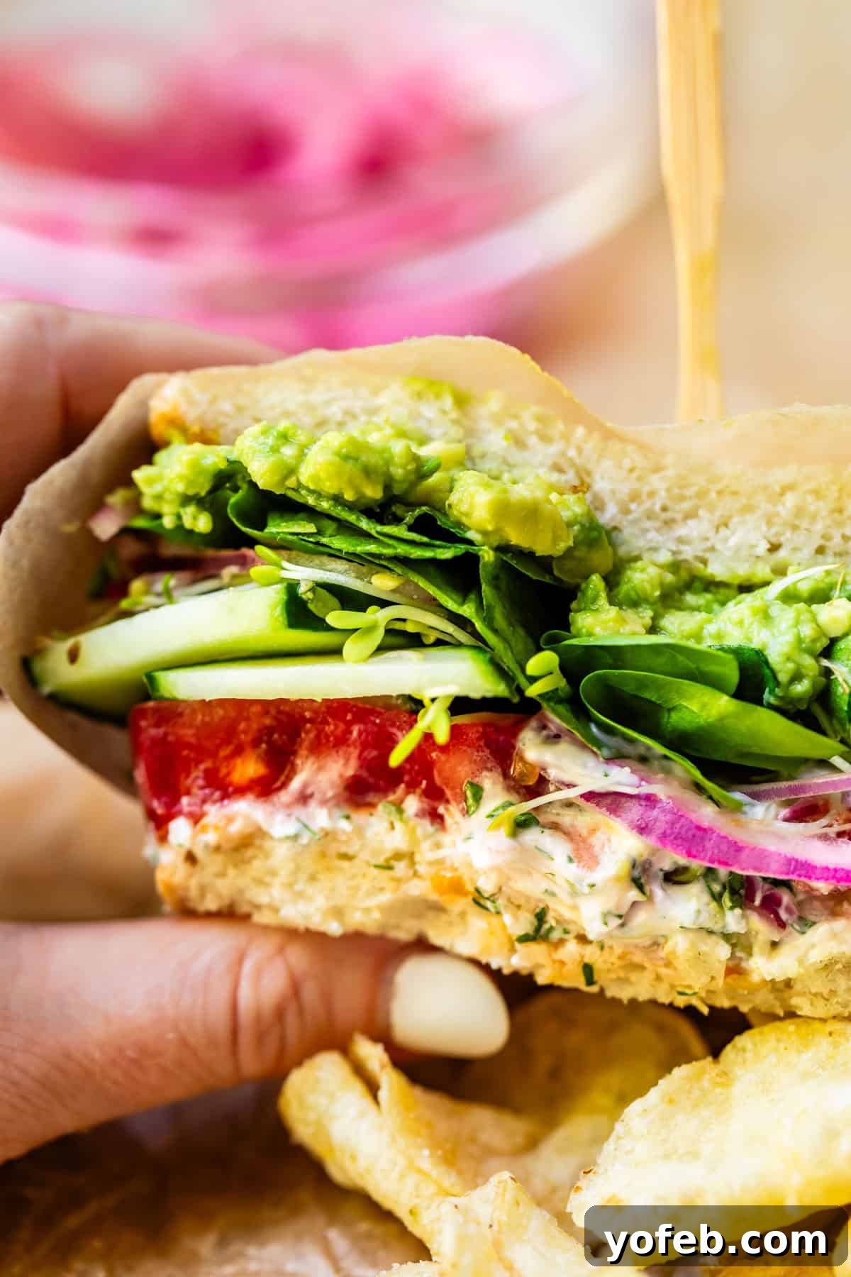 Vibrant Vegetable Stack 19 a hand holding a fresh veggie sandwich wrapped in parchment paper.