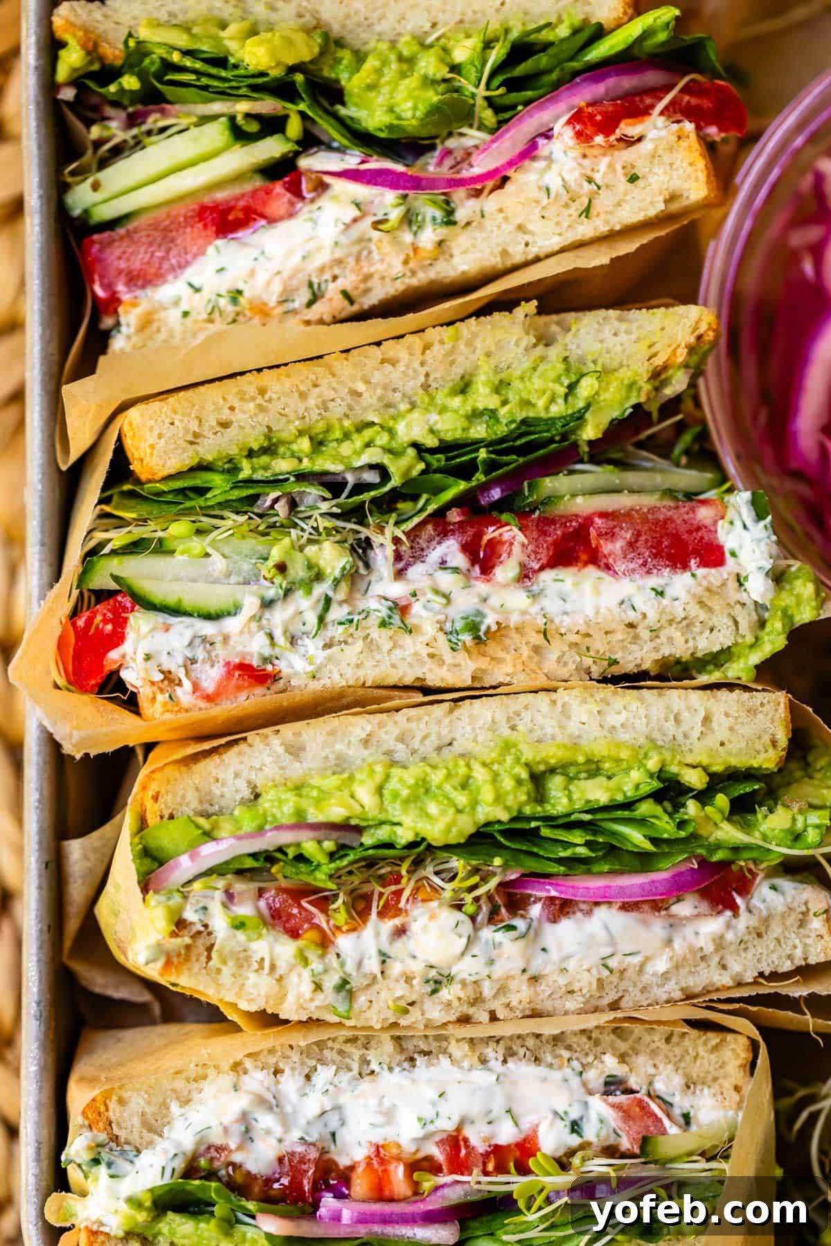 Vibrant Vegetable Stack 21 a metal baking tray filled with sideways stacked fresh vegetable sandwiches wrapped in parchment.