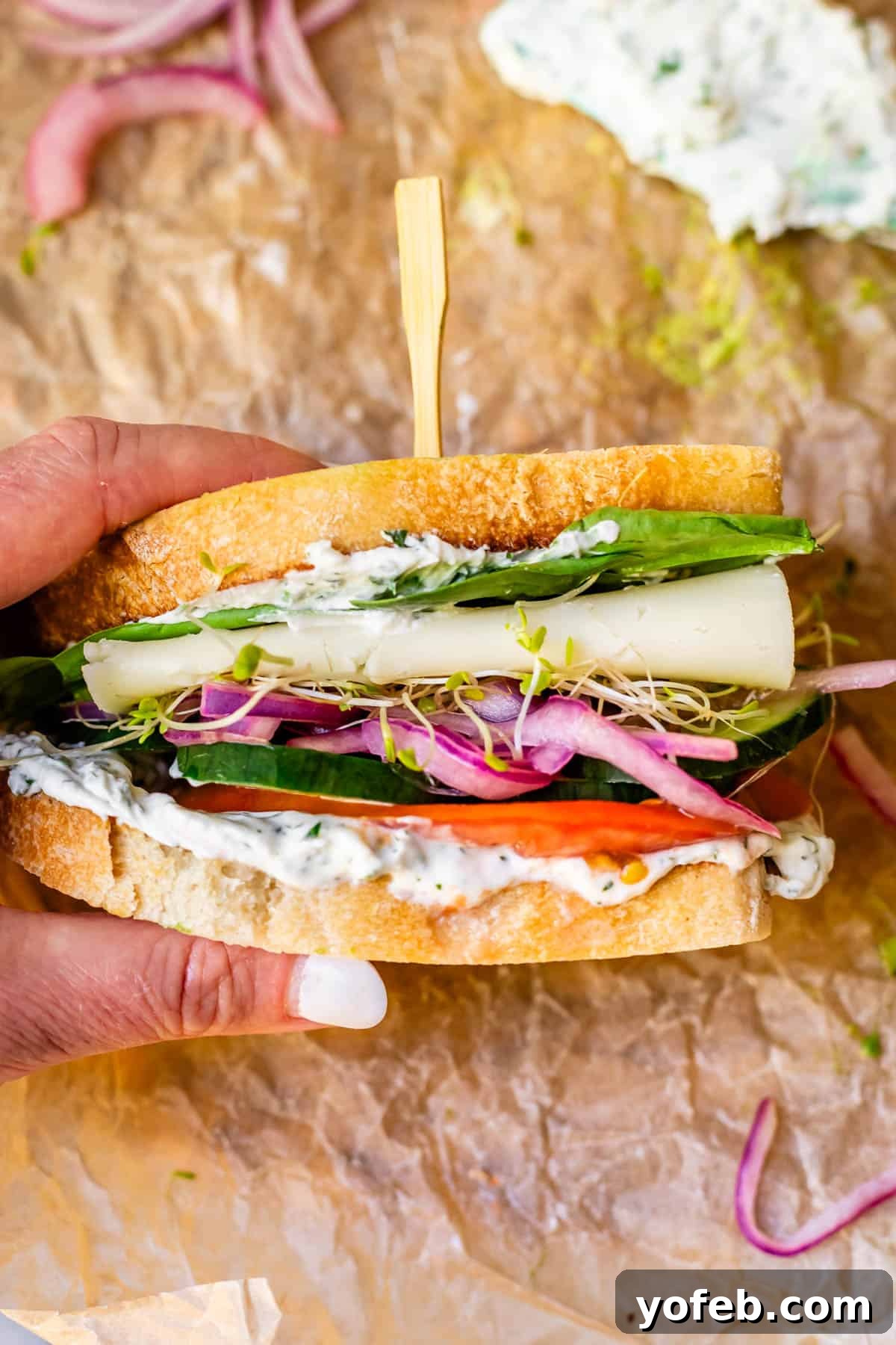 Vibrant Vegetable Stack 5 a hand holding one half of a vegetable sandwich with cheese, with a sandwich skewer in the top.