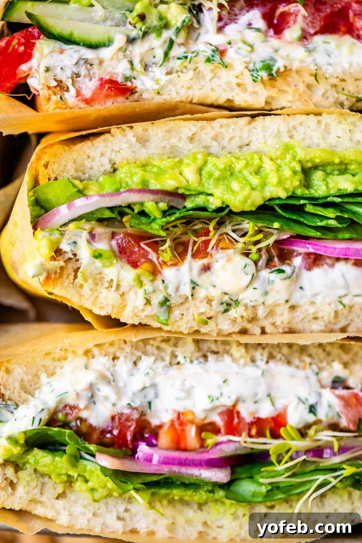 Vibrant Vegetable Stack 8 three veggie sandwiches wrapped in parchment paper stacked on top of each other.