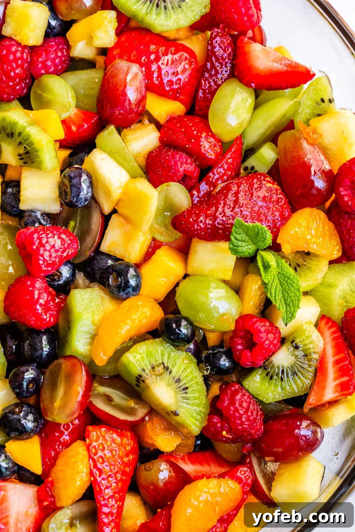 A glass bowl filled to the top with a vibrant, mixed fruit salad, glistening under a simple, homemade glaze. The colors are rich and inviting, promising a refreshing taste experience.