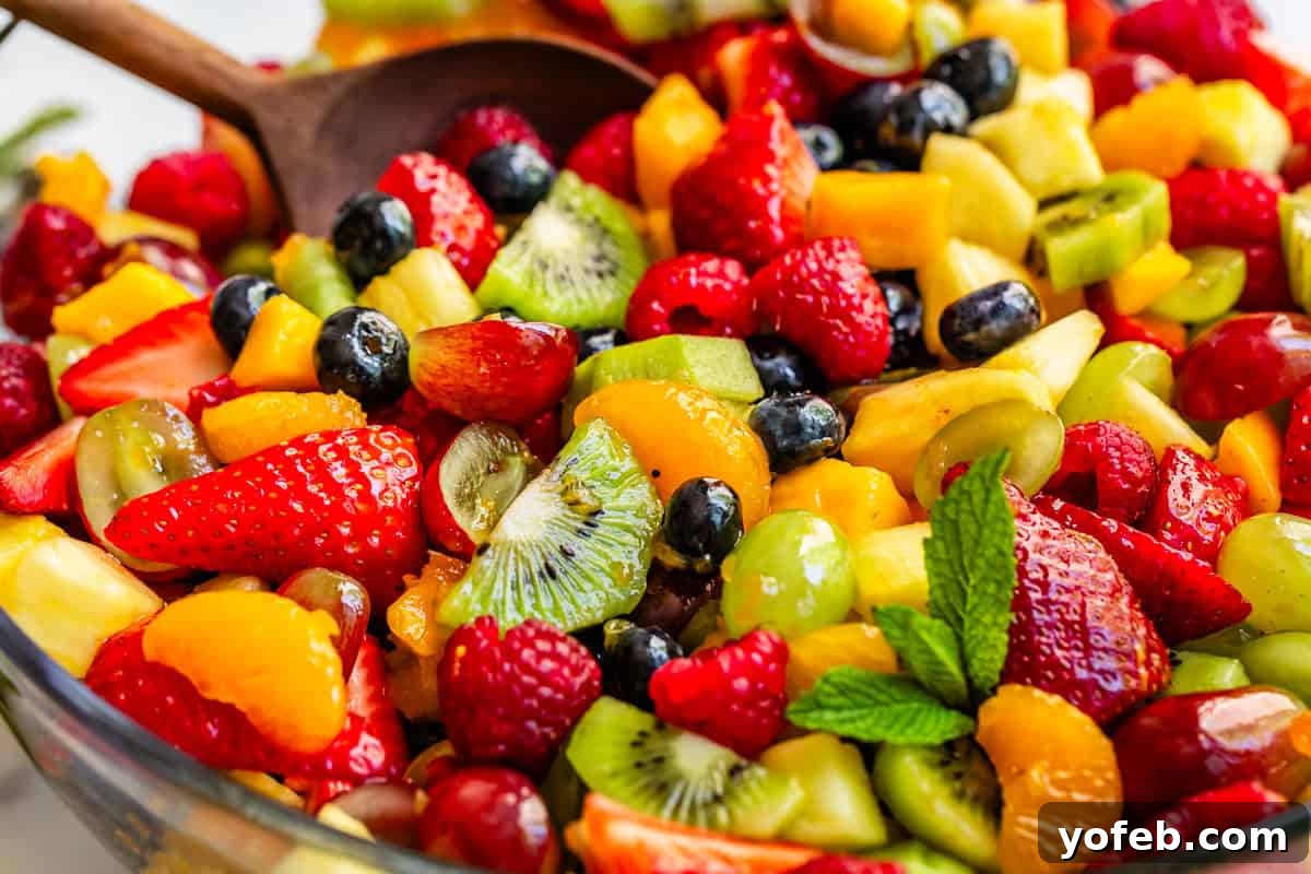 A large wooden spoon gently stirring a colorful, mixed fruit salad, perfectly coated with a simple, glistening glaze, in a glass bowl.