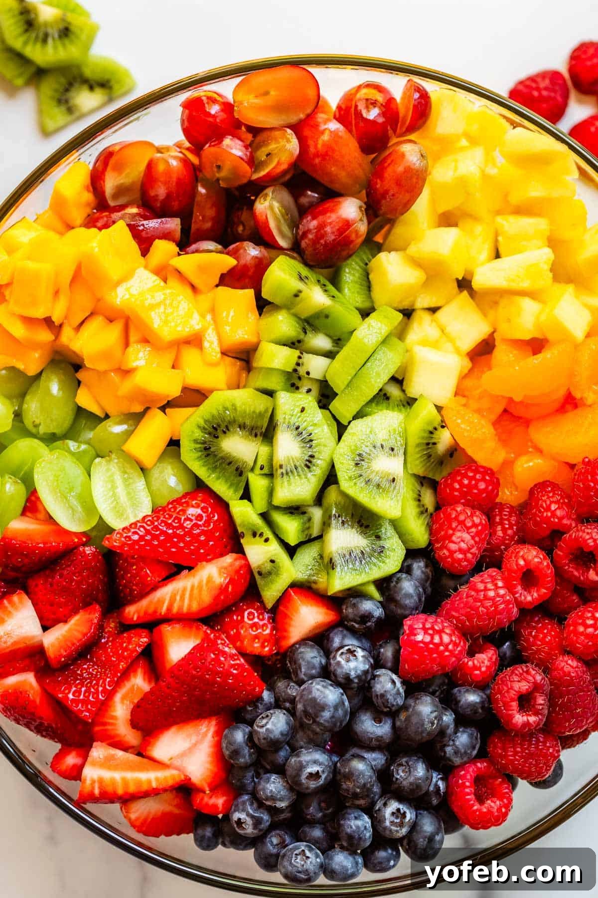 A large glass bowl overflowing with a delightful fruit salad, featuring luscious grapes, sweet raspberries, vibrant strawberries, and an assortment of other fresh fruits.