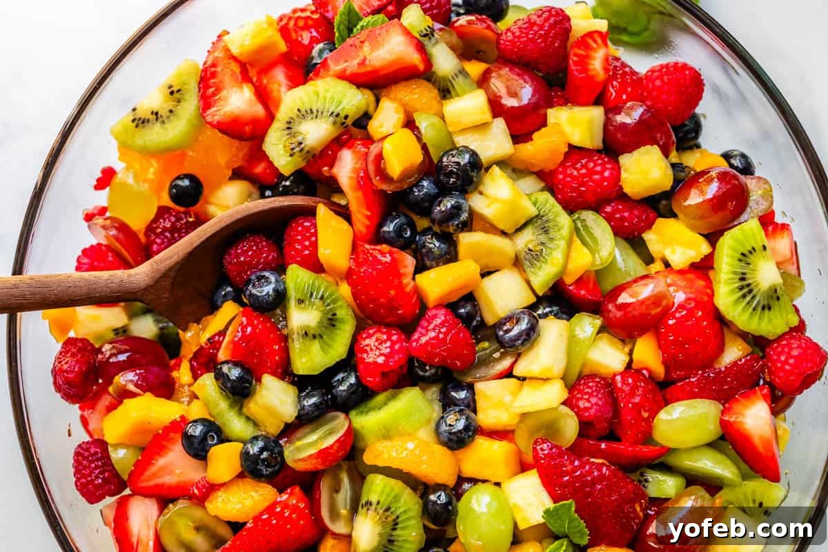 A pristine glass bowl showcasing a perfectly glazed fruit salad, with a wooden spoon resting inside, ready to be served. The fruits glisten under the light, indicating optimal freshness and flavor.