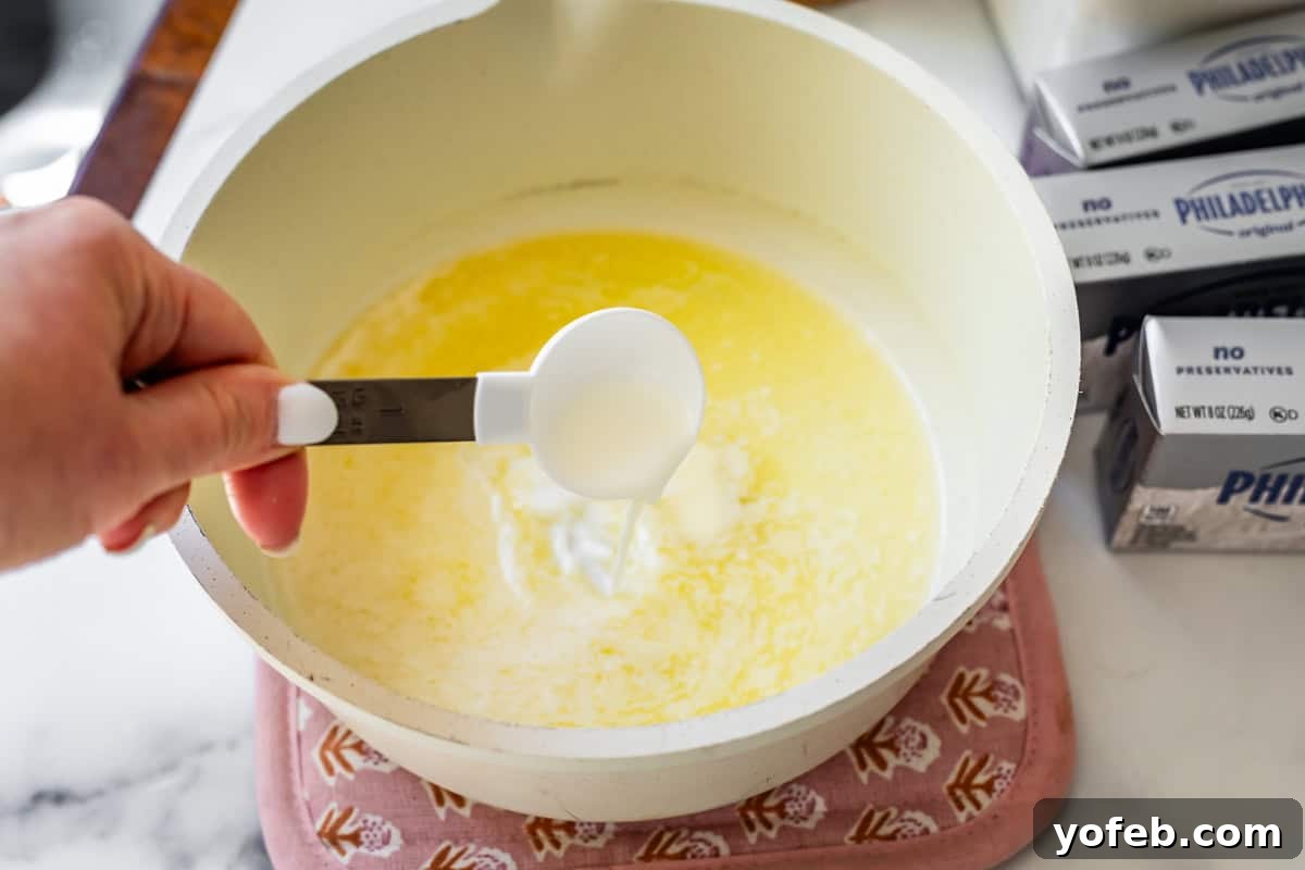 The Ultimate No Bake Cheesecake 21 a hand pouring milk from a measuring spoon into a pot with melted butter in it ready to be browned.