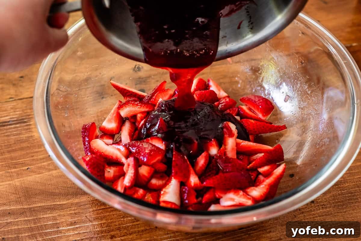 The Ultimate No Bake Cheesecake 30 a hand pouring warmed jam from a metal pan into a bowl with fresh topped strawberries.
