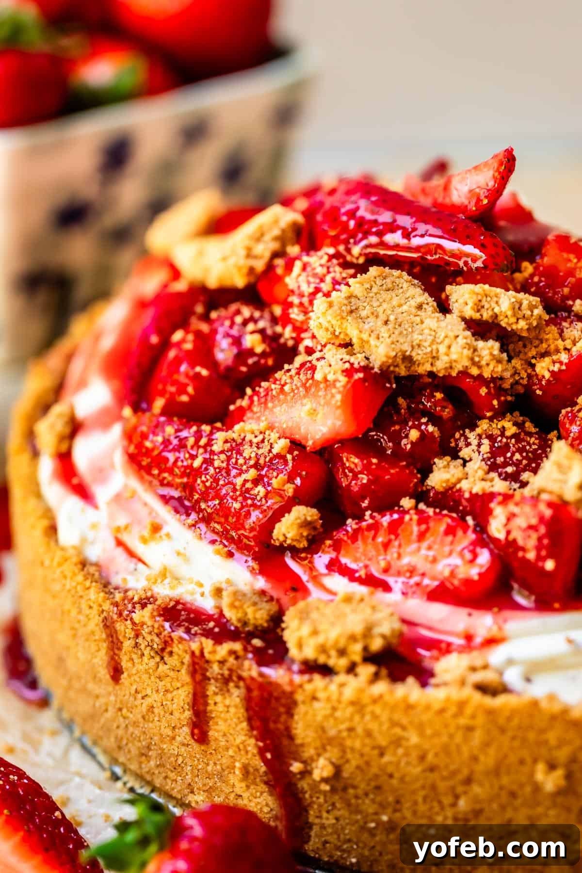 The Ultimate No Bake Cheesecake 32 side angle of no bake cheesecake with a heaping of fresh strawberry topping and graham crumble.