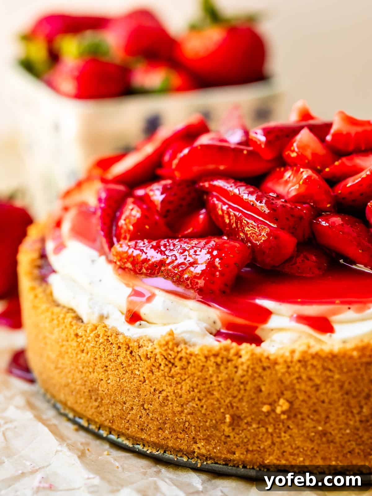 The Ultimate No Bake Cheesecake 36 side view of a whole no bake cheesecake smothered with fresh strawberry topping.
