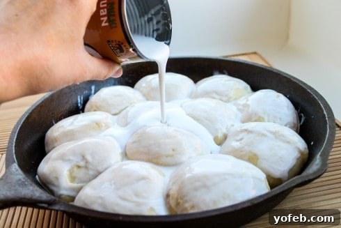 Coconut milk being poured generously over the risen rolls before baking.