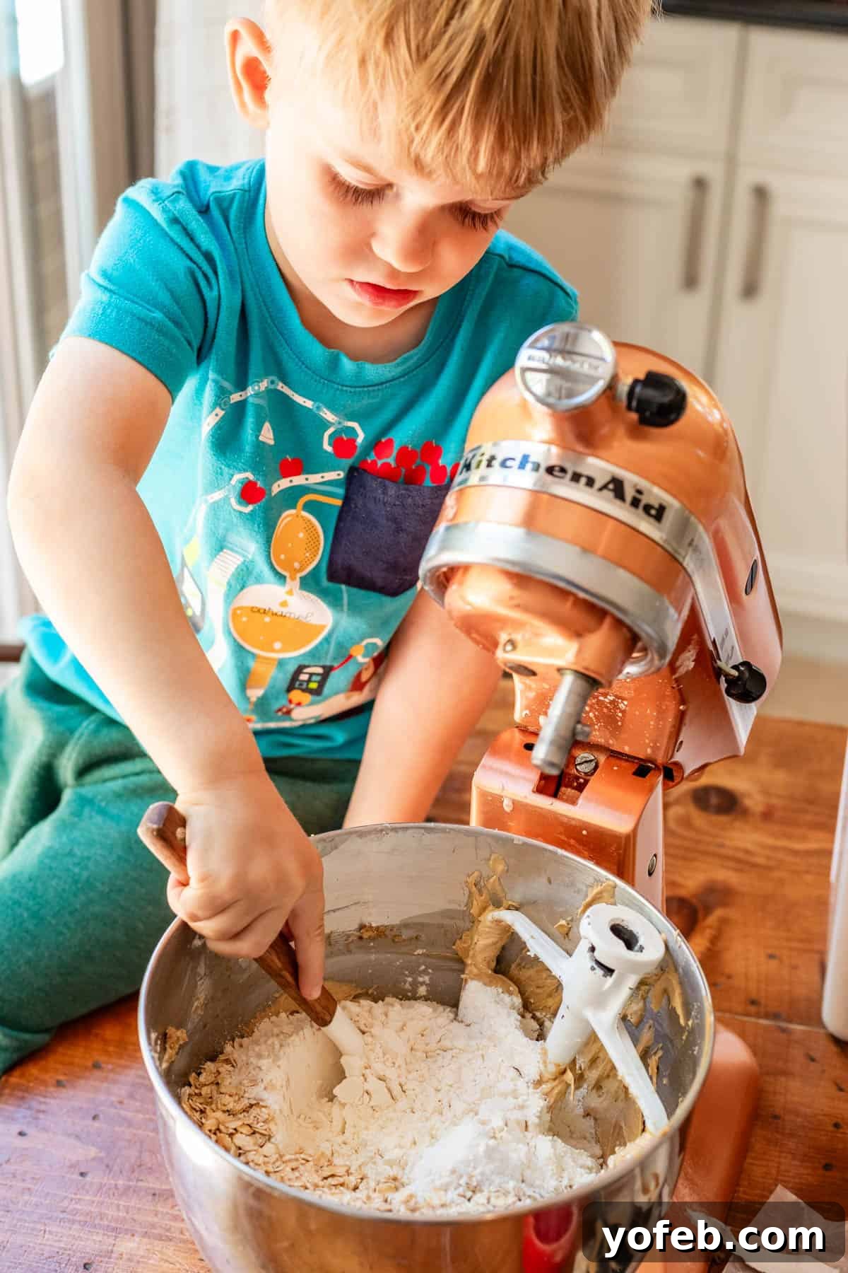 Classic Cafeteria Peanut Butter Bars 11 A small child enthusiastically using a spatula to mix flour into the oatmeal cookie dough batter in a large mixing bowl.