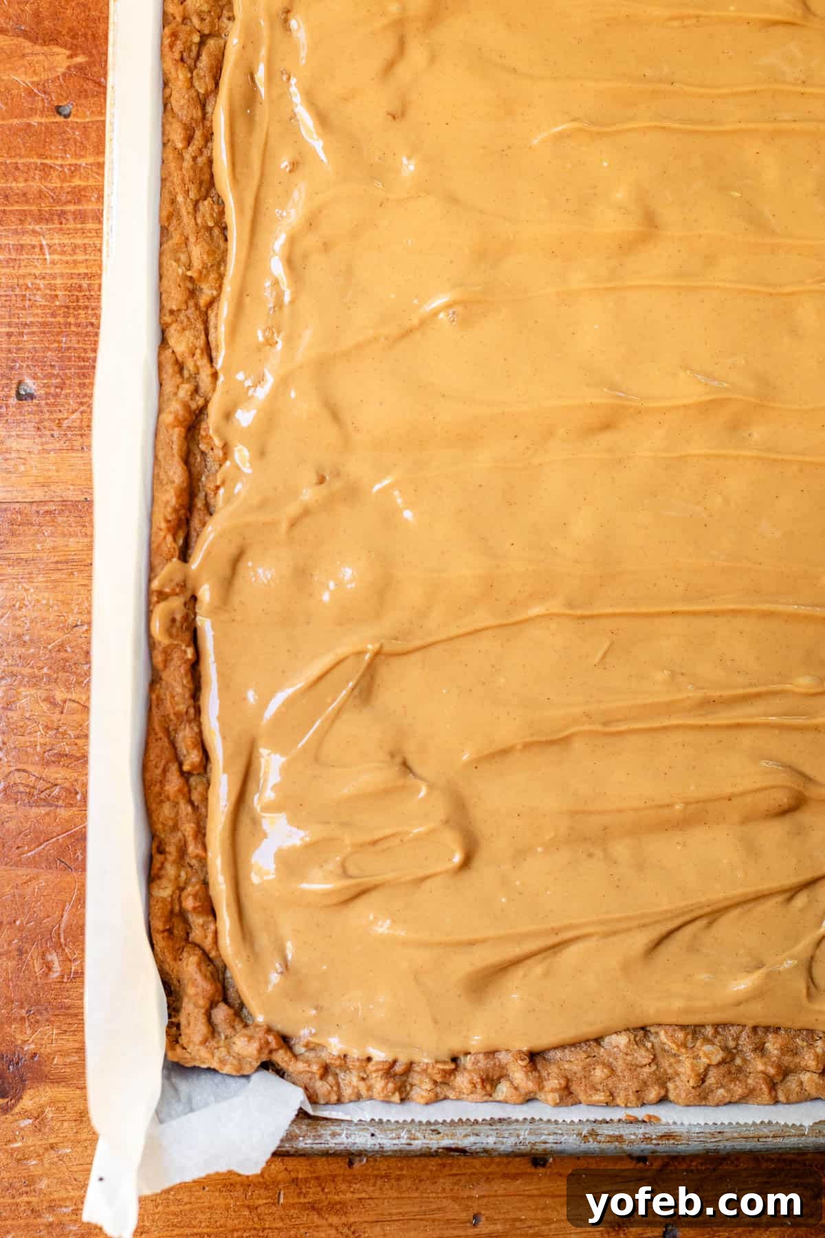 Classic Cafeteria Peanut Butter Bars 15 A baked oatmeal cookie dough base in a jelly roll pan, generously covered with an even layer of creamy peanut butter, cooling down before the next step.