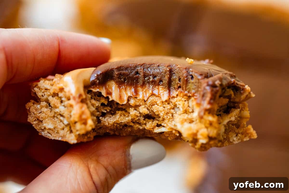 Classic Cafeteria Peanut Butter Bars 21 Fingers holding a single square of a Lunch Lady Peanut Butter Cookie Bar with a large bite taken out, revealing its soft and chewy texture.