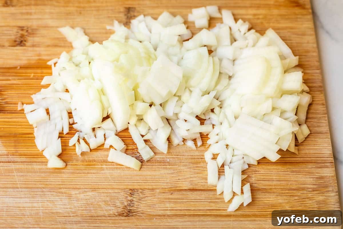 Chop Onions Like a Pro 11 a whole onion, chopped, on a wooden cutting board that is set on a countertop.