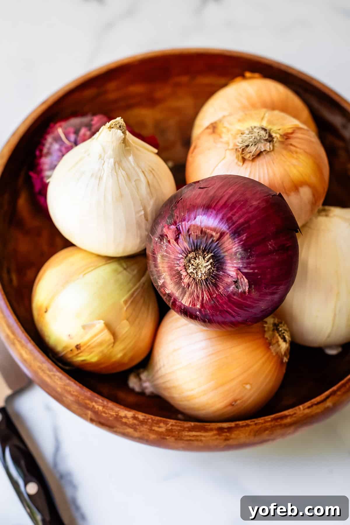 Chop Onions Like a Pro 3 wooden bowl filled with different onions, on a countertop next to a knife.