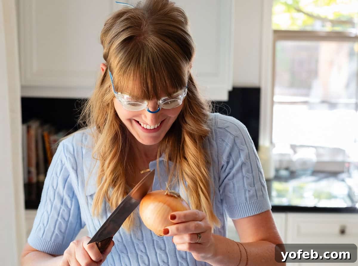 Chop Onions Like a Pro 5 woman wearing swim goggles using the back of a chefs knife to peel skin off an onion.
