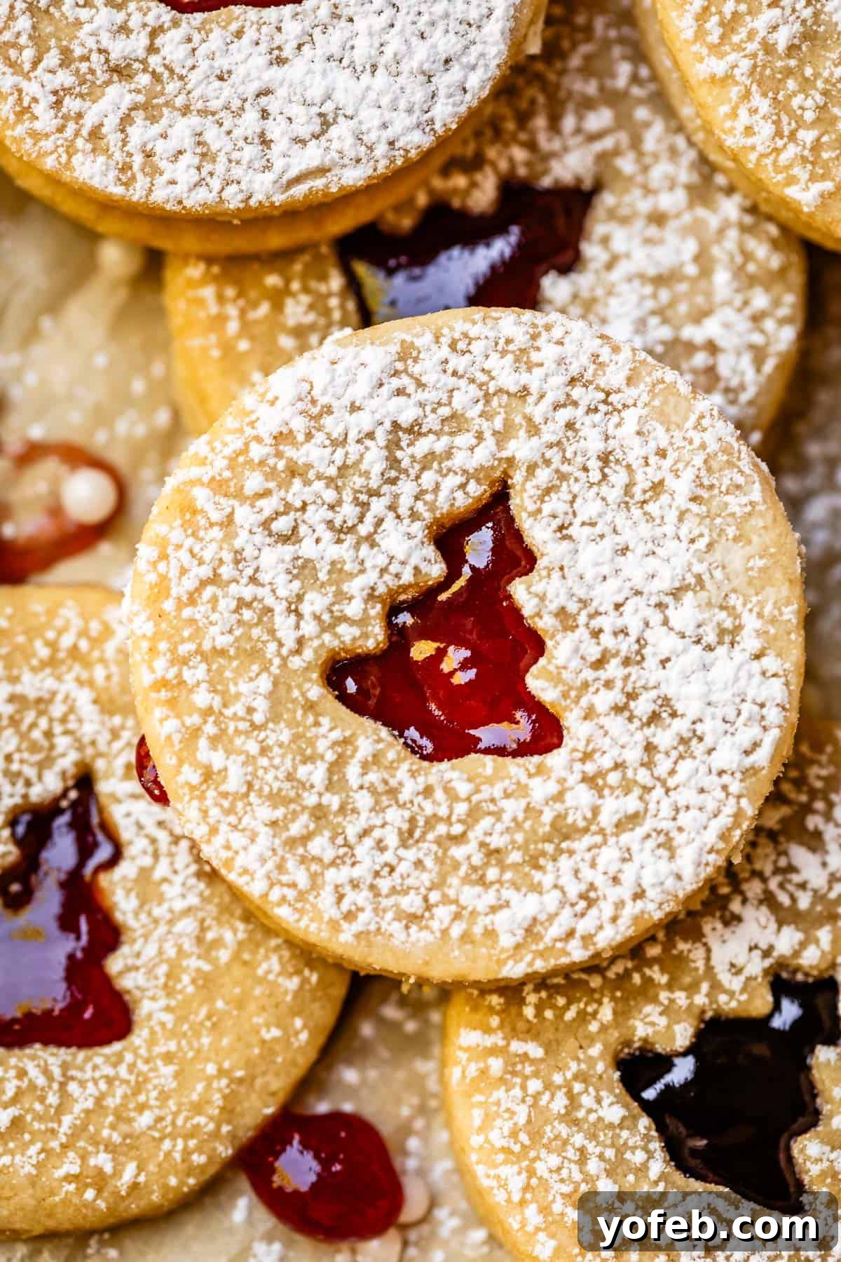 Melt-in-Your-Mouth Linzer Delights 2 Linzer cookie filled with vibrant raspberry jam peeking through a festive Christmas tree cutout, resting on a white platter.