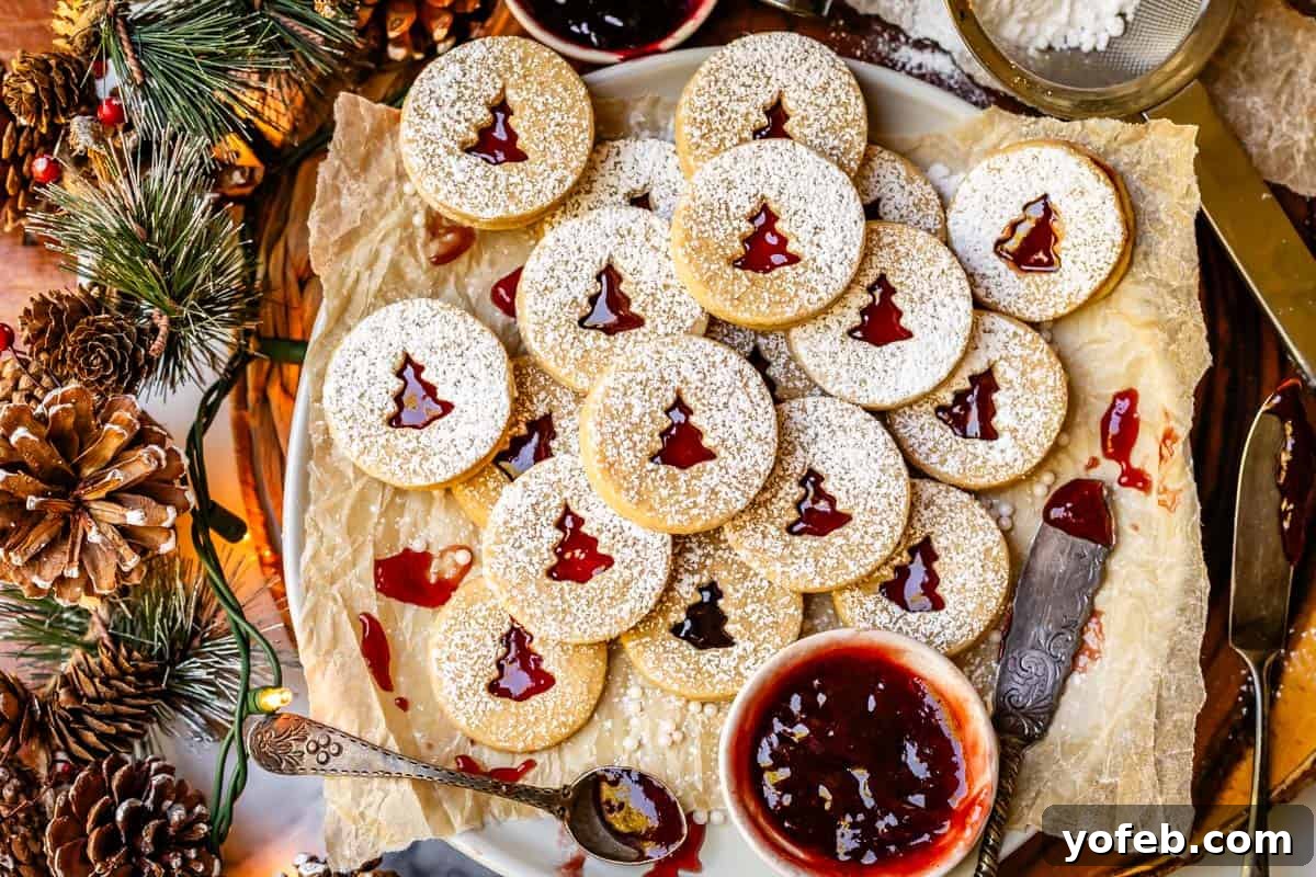 Melt-in-Your-Mouth Linzer Delights 18 A festive platter brimming with nearly 20 perfectly stacked Linzer cookies, accompanied by a small bowl of raspberry jam and a rustic pinecone garland in the background.