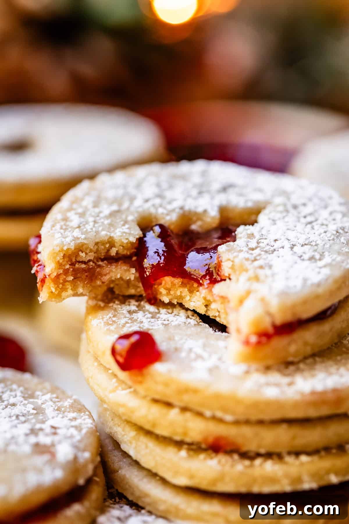 Melt-in-Your-Mouth Linzer Delights 20 A delicious Linzer cookie with a Christmas tree cutout and a vibrant jam filling, with a bite playfully taken from it.