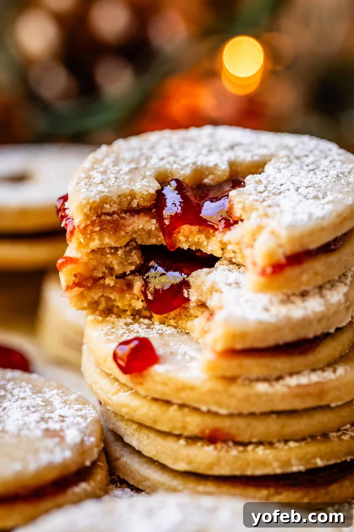 Melt-in-Your-Mouth Linzer Delights 3 A stack of beautifully crafted jam cutout Linzer cookies, with soft Christmas lights gently blurred in the background.
