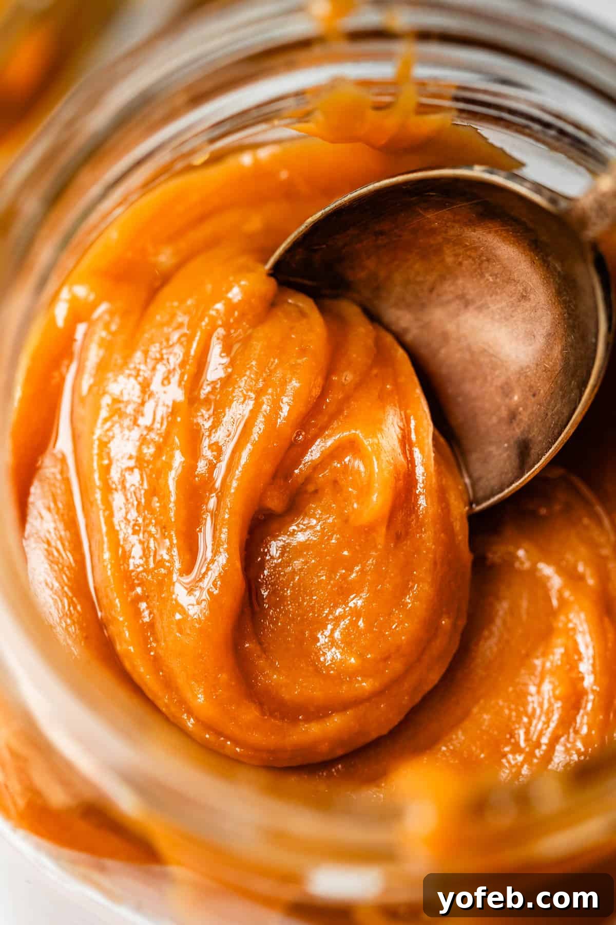 Dreamy Salted Caramel Sauce 3 A metal spoon gracefully dips into a glass jar, scooping up a generous portion of luscious caramel sauce, highlighting its thick, smooth texture.