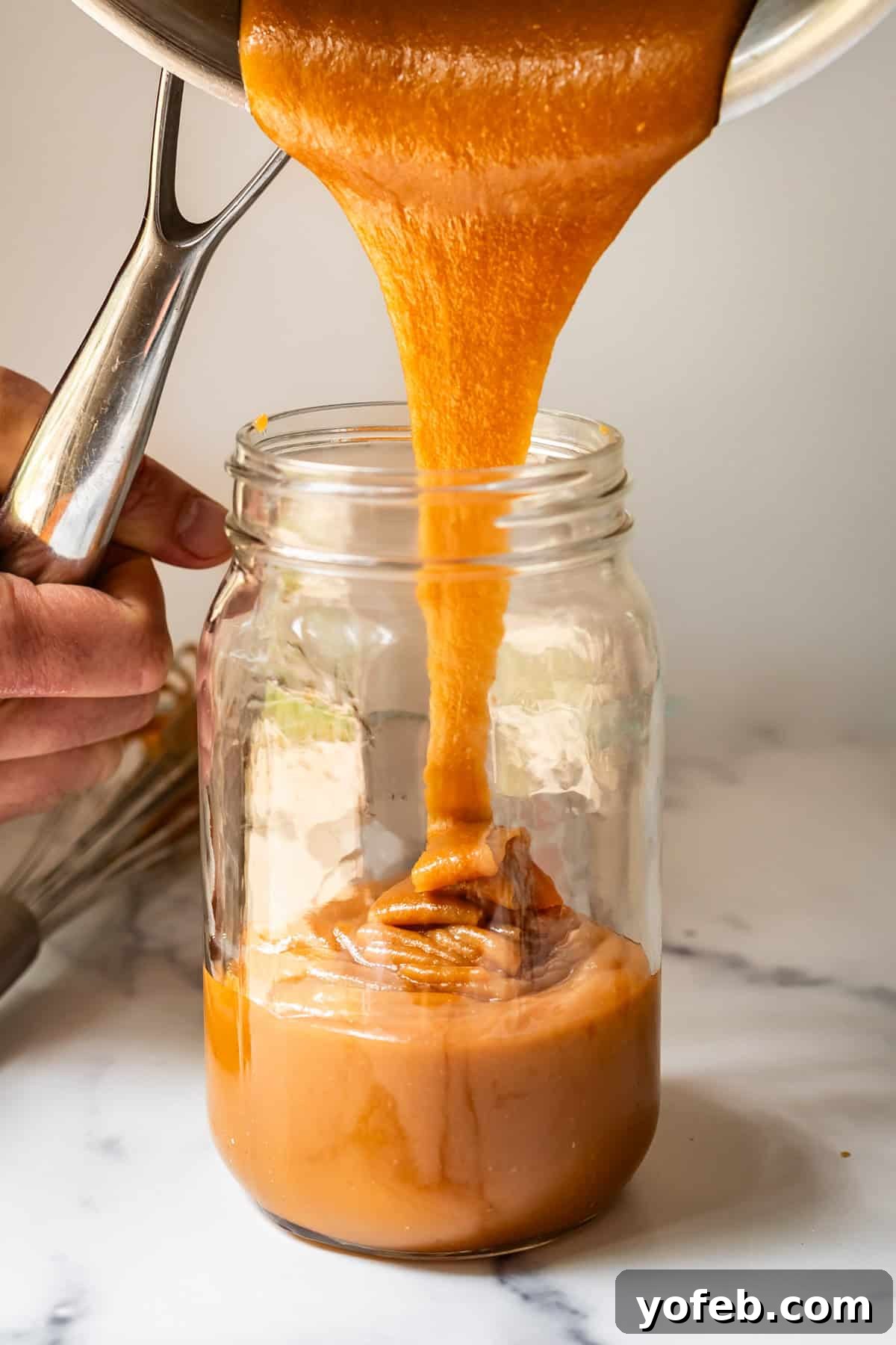 Dreamy Salted Caramel Sauce 23 Luscious salted caramel sauce being drizzled from a pan into a glass mason jar, showcasing its smooth flow and rich color.