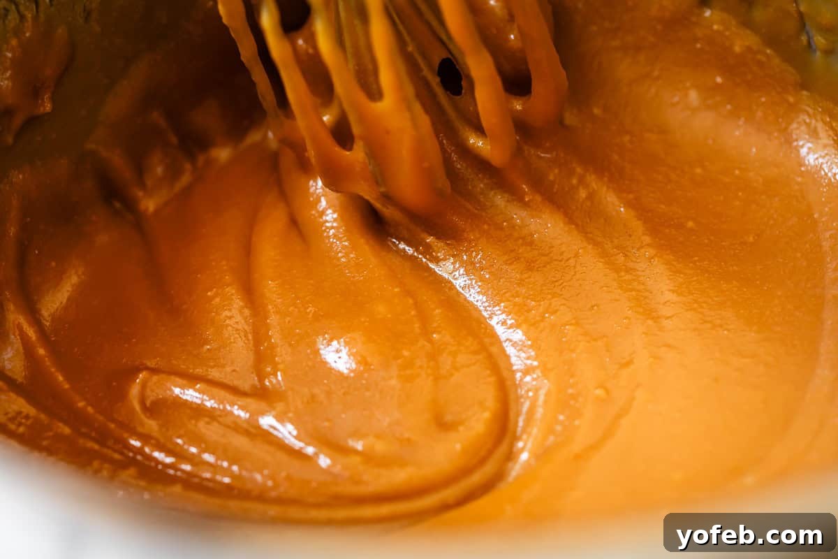 Dreamy Salted Caramel Sauce 9 A whisk stirs rich, amber caramel sauce in a pot, demonstrating the perfect consistency during cooking.