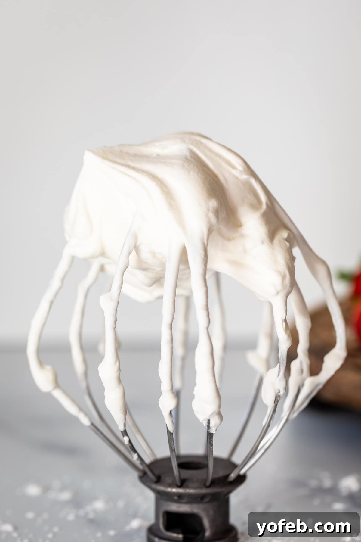 Homemade Whipped Cream Made Easy 11 whipped cream on a stand mixer whisk attachment on a marble counter.