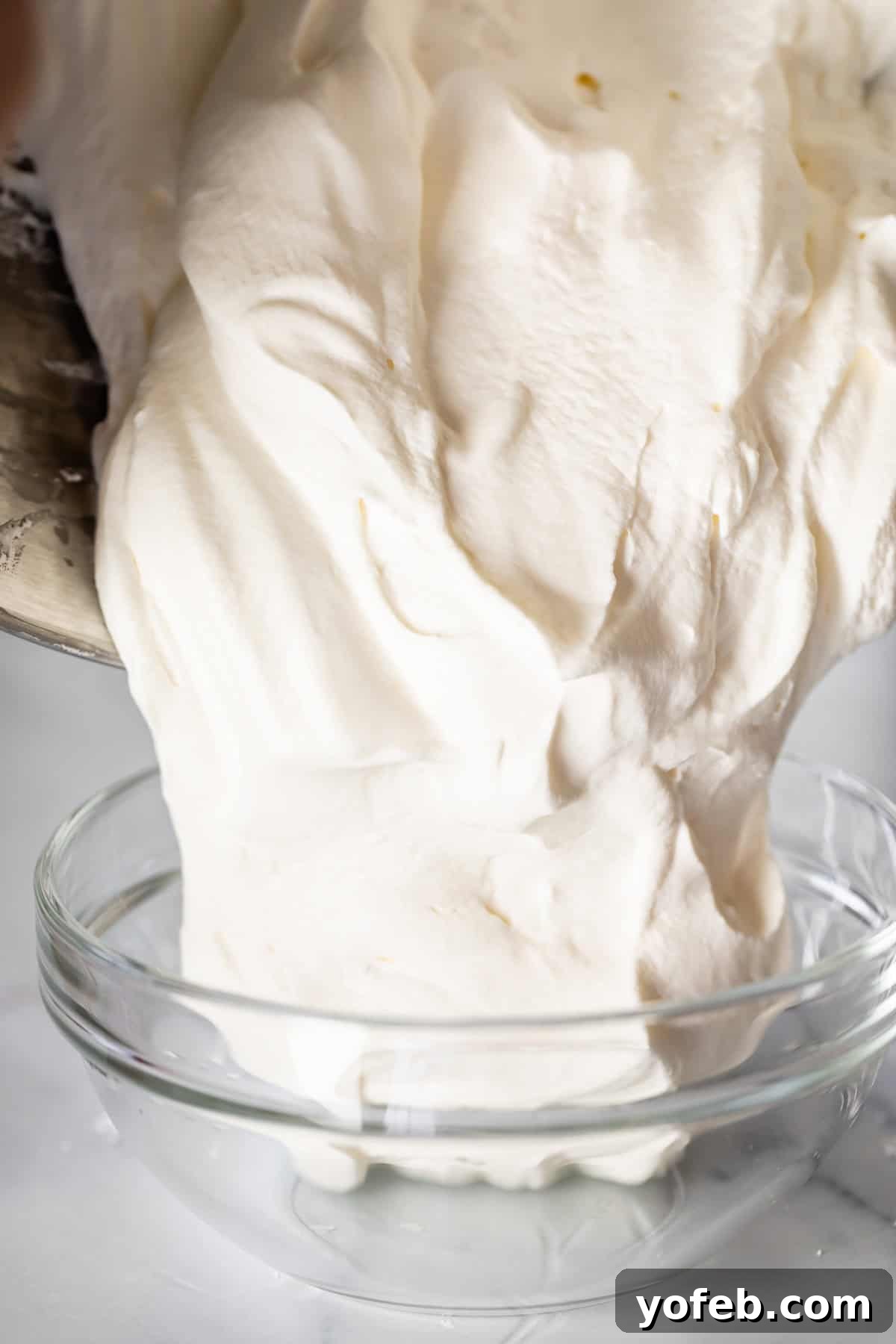 Homemade Whipped Cream Made Easy 12 pouring whipped cream from a metal mixer bowl into a glass bowl.
