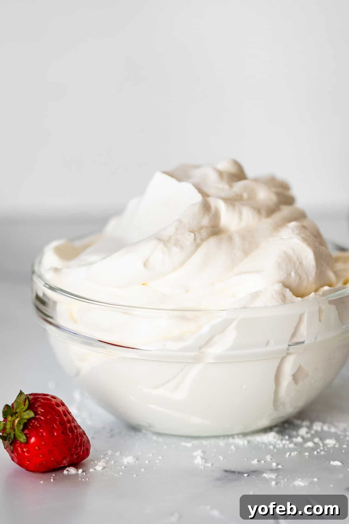 Homemade Whipped Cream Made Easy 14 glass bowl with whipped cream and single strawberry on marble counter .