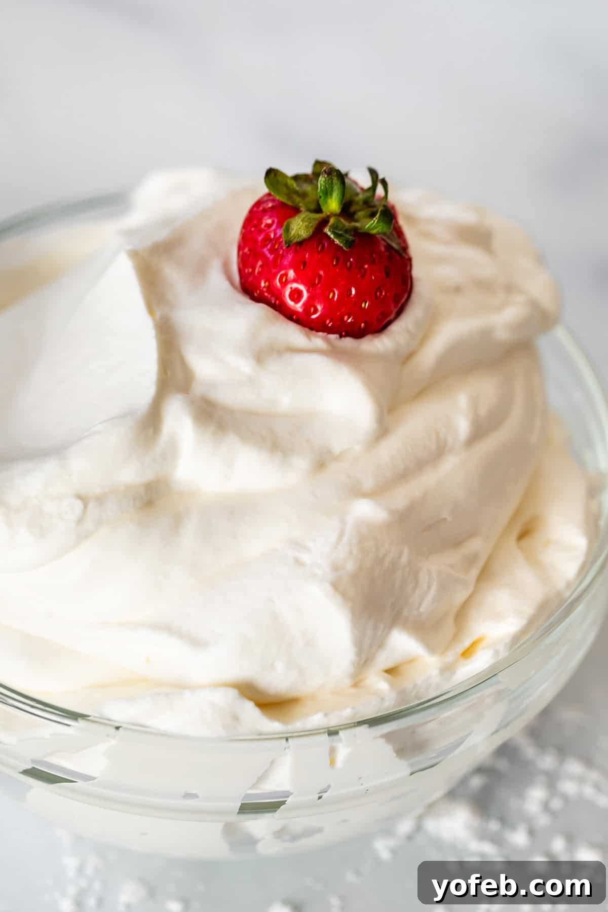 Homemade Whipped Cream Made Easy 18 glass bowl filled over the top with pillowy whipped cream, with a strawberry in the top.