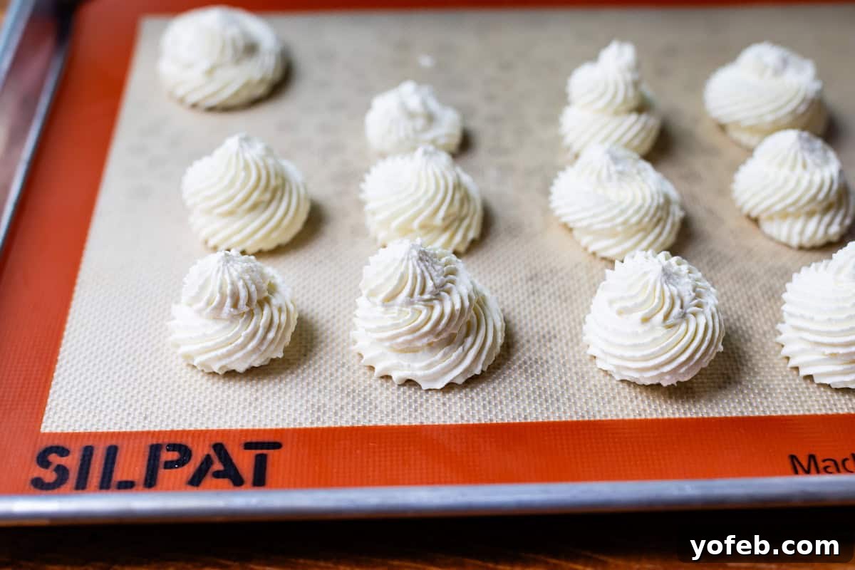 Homemade Whipped Cream Made Easy 20 whipped cream piped into individual swirls on a silpat on a baking sheet.